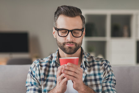 Photo of young handsome stubble man happy positive enjoy aroma morning cup of coffee break pause indoorsの写真素材