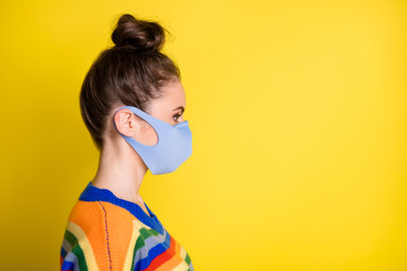 Profile side photo of pretty lady social distance wear mask look empty space isolated on shine yellow color backgroundの写真素材