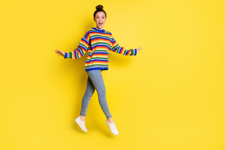 Full body photo of cheerful charming lady wear rainbow color sweater jump up isolated on yellow...