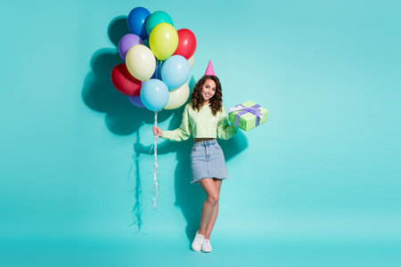 Photo of lovely girl hold present bunch balloons wear green sweater jeans mini skirt cone hat...