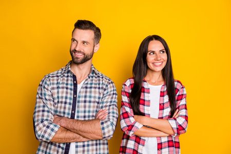 Portrait of attractive cheerful minded couple folded arms thinking clue isolated over bright yellow...