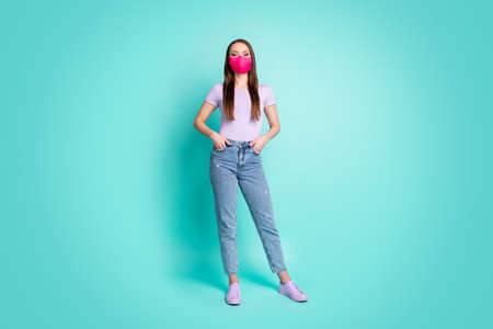 Full length body size portrait of girl wearing pink protective mask keeping hands in pockets isolated on vibrant teal color backgroundの写真素材