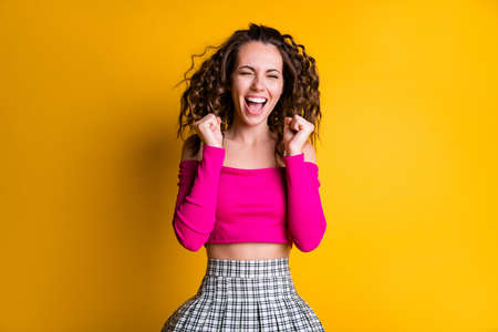 Photo portrait of excited woman holding fists up screaming wearing pink crop-top plaid skirt isolated on bright yellow colored backgroundの写真素材