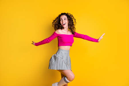 Photo portrait of woman skipping jumping standing on one leg hands to sides open mouth wearing fuchsia crop-top plaid skirt knee-high socks isolated on bright yellow colored backgroundの写真素材