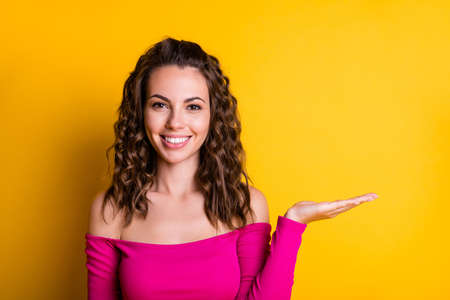 Photo portrait of pretty girl holding hand palm new product blank space smiling wearing fuchsia crop-top isolated on bright yellow colored backgroundの写真素材