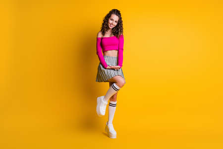 Full body photo cute charming coquettish curly lady hands lift knee wear pink naked shoulders top short checkered skirt white socks sneakers isolated vivid yellow color backgroundの写真素材