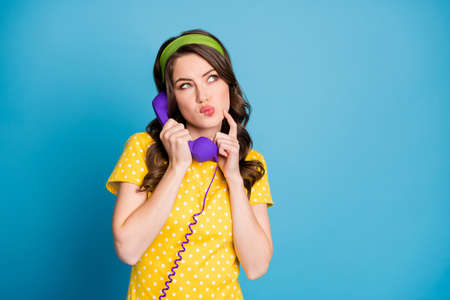 Photo portrait of woman touching face with finger holding purple phone isolated on pastel light blue...