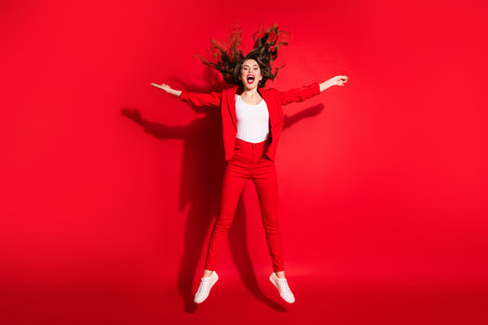 Full length profile photo of charming young lady jump star pose open mouth wear blazer trousers footwear isolated red color backgroundの写真素材