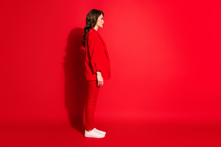 Full size profile side photo of gorgeous sweet lady stand isolated over shine red color background look into empty spaceの写真素材