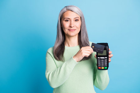 Photo of glad aged lady hold credit card show pos terminal reading machine wear casual isolated over blue color backgroundの写真素材