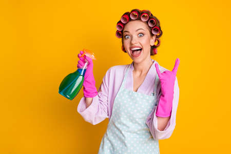 Crazy girl use chemical spray bottle show horned symbol wear bath robe gloves isolated yellow color backgroundの写真素材