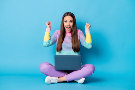 Portrait of pretty glad cheerful girl sitting lotus position crossed legs using laptop having fun isolated over bright blue color backgroundの写真素材