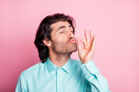Photo portrait of man showing chefs kiss isolated on pastel pink colored backgroundの写真素材