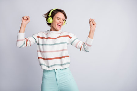 Photo of cute sweet young lady wear striped sweater earphones singing dancing arms hands fists isolated grey color backgroundの写真素材