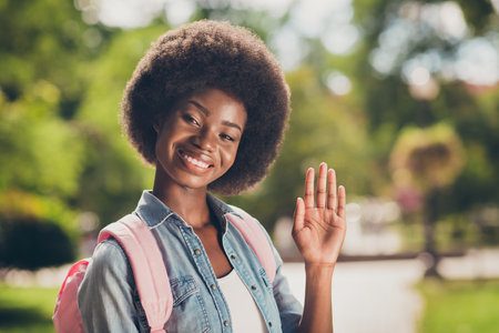 Photo portrait of black skinned young woman with curly hairstyle smiling greeting waving with palm...