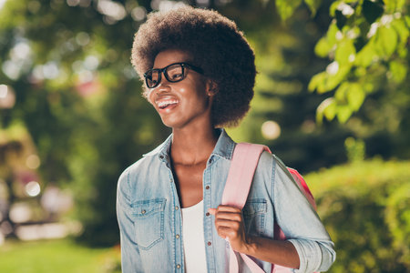 Photo portrait of pretty nice black skinned curly girl laughing cheerfully wearing fashionable glasses jeans shirt backpackの写真素材