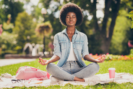 Photo portrait of black skinned young woman sitting in city green park near bag doing yoga asana lotus having pause chill rest closed eyesの写真素材