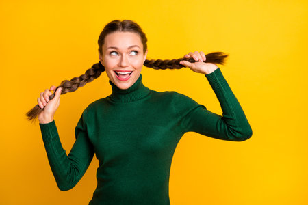 Photo portrait girl cheerful childish looking blank space smiling touching braids isolated vivid yellow color backgroundの写真素材