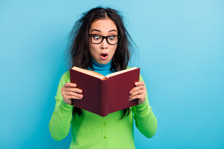 Photo of surprised amazed young woman hold read book unbelievable novel isolated on shine blue color...