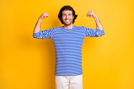 Photo of positive middle eastern man show muscles on arms wear nautical vest isolated over yellow color backgroundの写真素材