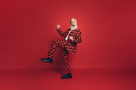 Photo of excited gentleman raise fists knee celebrate open mouth wear heart print tux shoes isolated red backgroundの写真素材