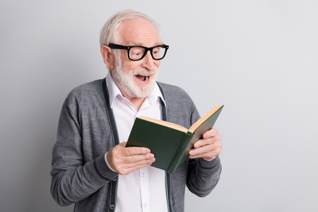 Portrait of old white hair impressed man read book wear spectacles dark sweater isolated on grey...