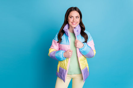 Photo of young cheerful girl happy positive smile dream dreamy look empty space windbreaker isolated over blue color backgroundの写真素材