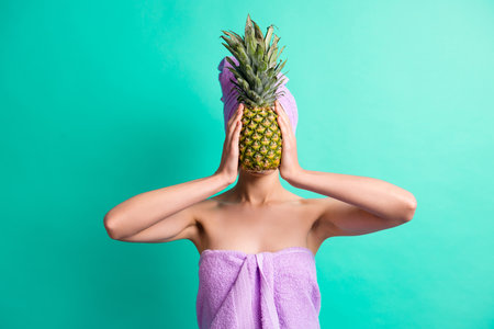 Photo of girl hands hold pineapple cover hide face wear purple towel turban isolated turquoise color...