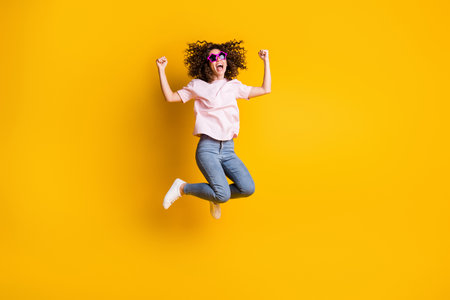 Photo portrait full body view of successful woman jumping up isolated on vivid yellow colored backgroundの写真素材