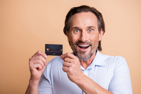 Photo of funny excited man presenting debit card look camera open mouth wear shirt isolated beige color backgroundの写真素材
