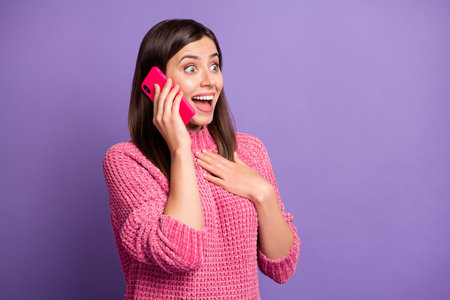Photo portrait of amazed girl talking on mobile phone touching chest staring at blank space isolated on vivid purple color backgroundの写真素材