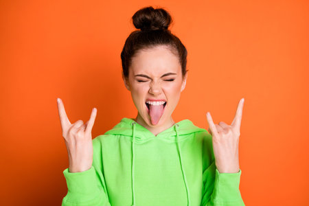 Photo portrait of crazy girl showing tongue two rock goat signs isolated on vivid orange colored backgroundの写真素材
