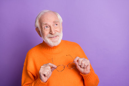 Photo of cheerful aged man arms hold eyewear look interested empty space imagine isolated on violet color backgroundの写真素材
