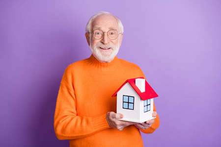 Photo of positive aged man hands hold little house beaming smile isolated on violet color backgroundの写真素材
