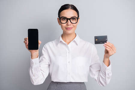 Photo of lady hold phone screen empty space show credit card wear specs white shirt isolated grey color backgroundの写真素材
