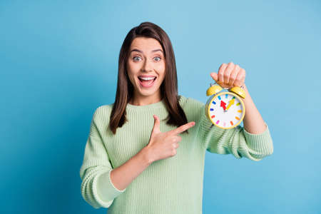 Photo of astonished girl point index finger clock wear green sweater isolated over blue color backgroundの写真素材