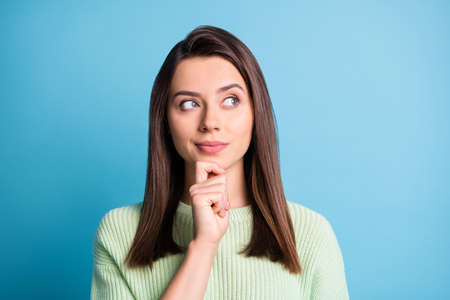 Photo of minded pretty girl arm chin look up empty space wear green pullover isolated blue color backgroundの写真素材
