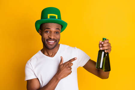 Photo of attractive dark skin guy hold beer alcohol beverage students party saint patrick day direct finger two bottles wear casual white t-shirt isolated bright yellow color backgroundの写真素材