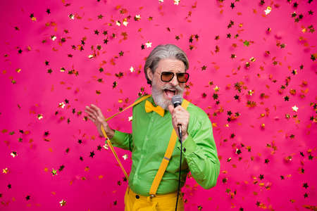 Photo of funny aged grandpa club party singing karaoke microphone confetti fall excited singer wear sun specs green shirt yellow suspenders tie isolated shine pink color backgroundの写真素材