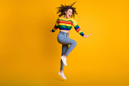 Full length photo of funny jumping woman dressed casual colorful sweatshirt looking empty space isolated yellow color backgroundの写真素材