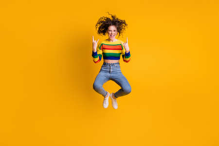 Full length photo of funny jumping woman dressed casual colorful sweatshirt showing hard rock sign isolated yellow color backgroundの写真素材