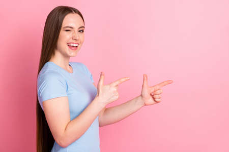 Photo portrait profile of winking girl pointing two fingers to side isolated on pastel pink colored...