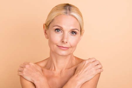 Close up photo of attractive charming middle aged woman hug herself isolated beige color background