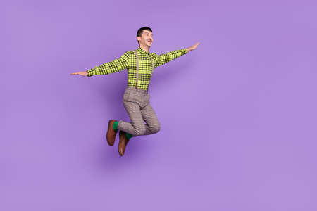 Full size profile side photo of young happy excited positive good mood man jumping hands wings isolated on violet color backgroundの写真素材