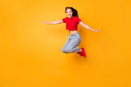 Full length photo of crazy jumping high lady wear red crop top jeans shoes isolated yellow color...