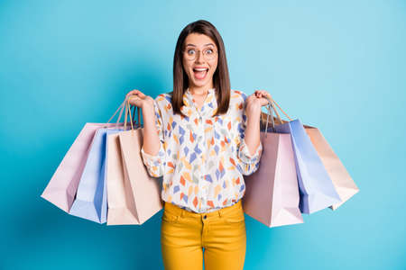 Photo of pretty lady hold many mall bags wear eyewear geometry print shirt yellow trousers isolated blue color backgroundの写真素材