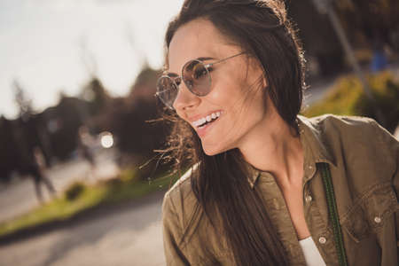 Profile side photo of sweet cute shiny young lady wear brown shirt dark glasses smiling outside sunny streetの写真素材