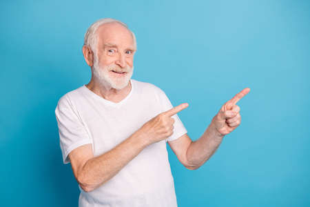Photo portrait of old man pointing two fingers at blank space isolated on pastel blue colored...