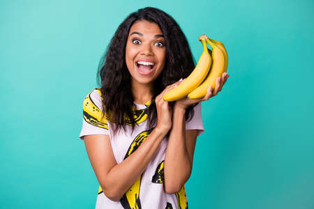 Photo of astonished dark skin girl scream hold bananas wear pink t-shirt isolated over teal color...