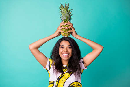 Photo of carefree dark skin girl hold pineapple head wear pink t-shirt isolated over teal color...